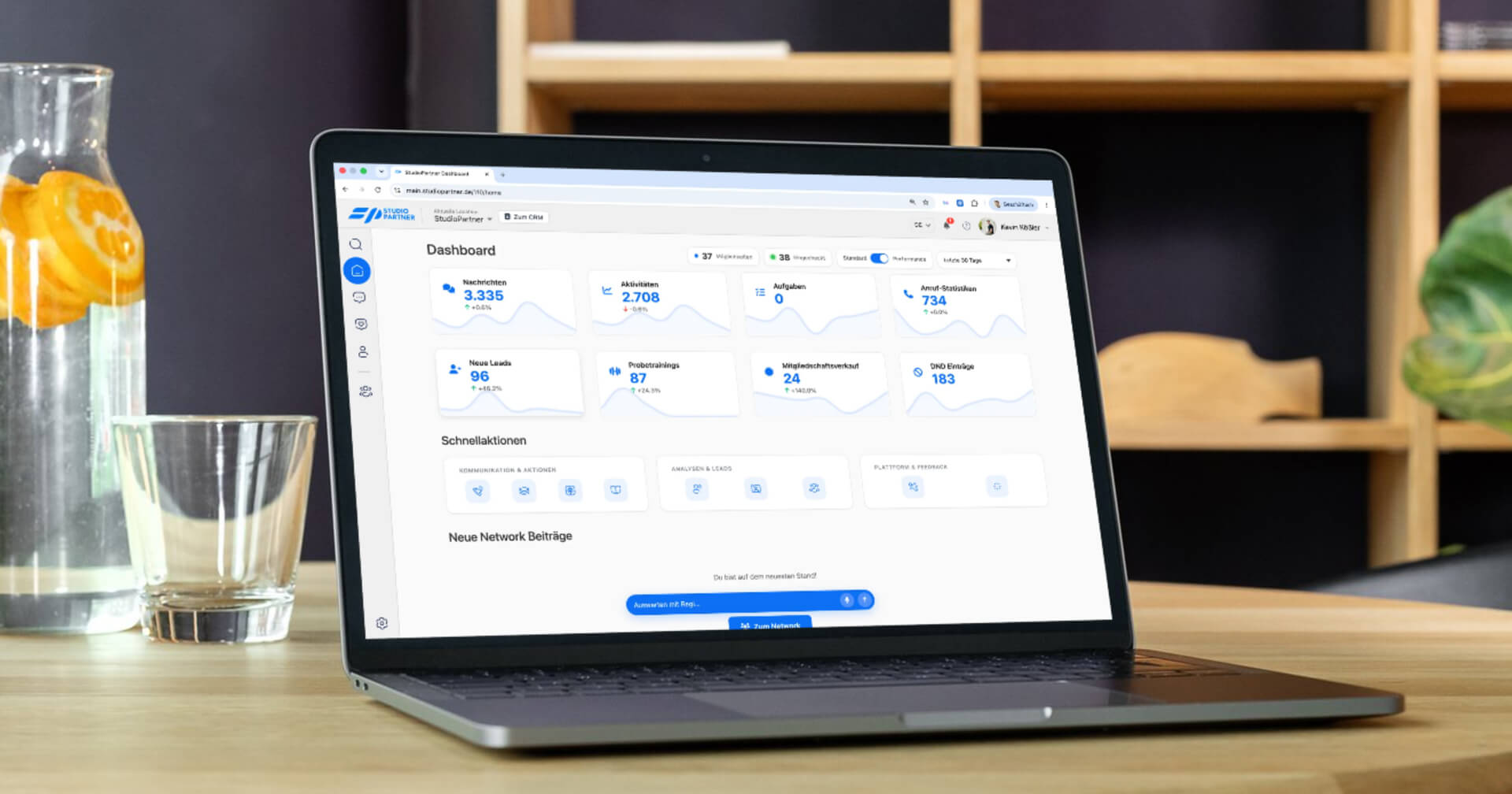 Ein aufgeschlagenes Laptop auf einem Holztisch zeigt ein digitales Studio-Partner-Dashboard mit Kennzahlen.