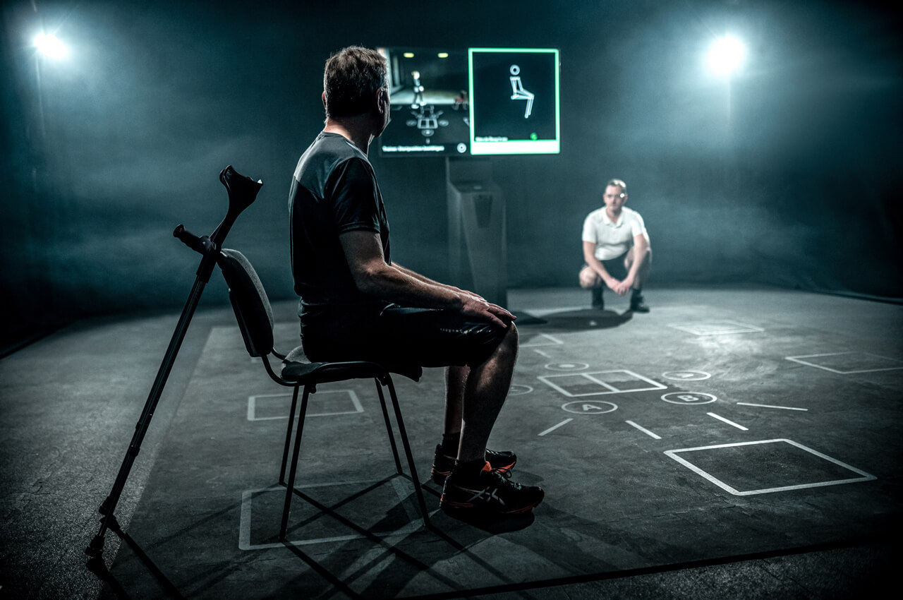 Patient sitzt auf einem Stuhl mit Physiotherapeut und wird vom Skillcourt gescannt