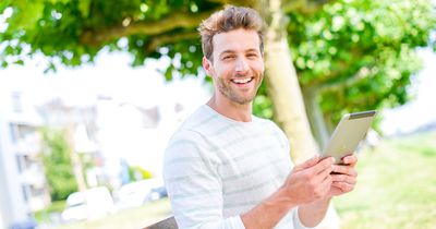 Student sitzt in einem Park mit einem Tablet in der Hand