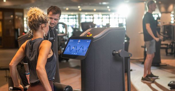 Frau trainiert unter Aufsicht eines Trainers an einem Fitnessgerät