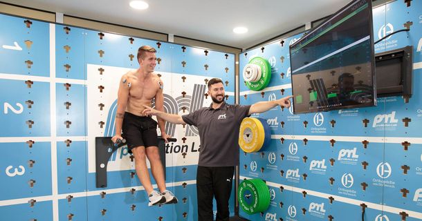 Mann macht oberkörperfrei mit Elektroden Dips an der Wand von Cube Sports, Trainer zeigt ihm Ergebnisse auf Bildschirm