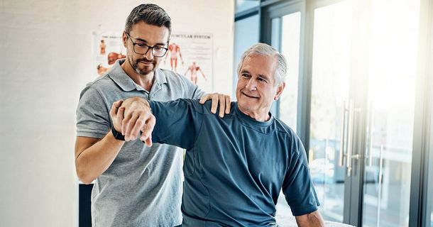 Älterer Physiotherapeut behandelt älteren Patienten an der Schulter