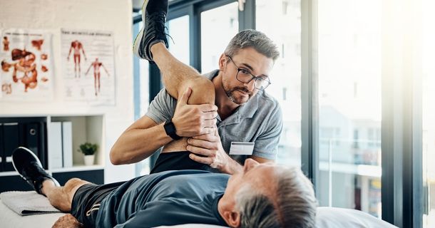 Physiotherapeut behandelt das Bein eines Patienten auf der Liege