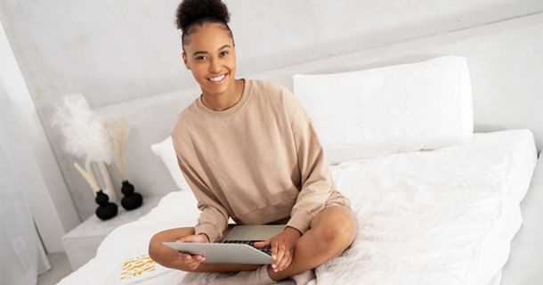 Dunkelhäutige, lächelnde Frau auf Bett mit Tablett