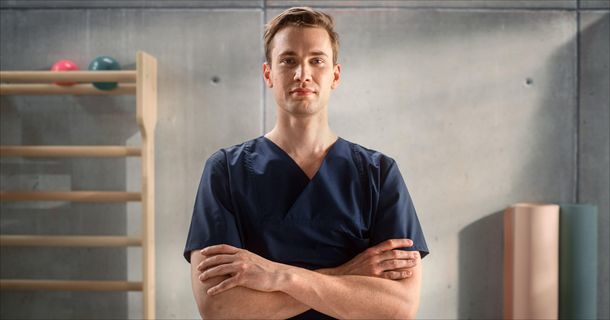 Physiotherapeut in Arztkittel vor einer Sprossenwand in Therapieraum