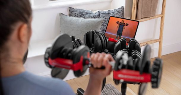 Mann trainiert zu Hause mit BowFlex Hantel vor Bildschirm 
