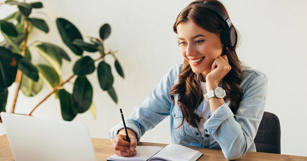 Porträt einer jungen lächelnden Frau mit Kopfhörern, die an einem Webinar im Büro teilnimmt.