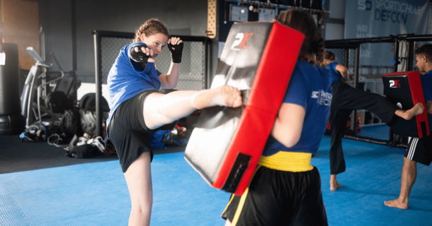 In einem Fitnessstudio kickt eine Kickboxerin auf eine Matte.