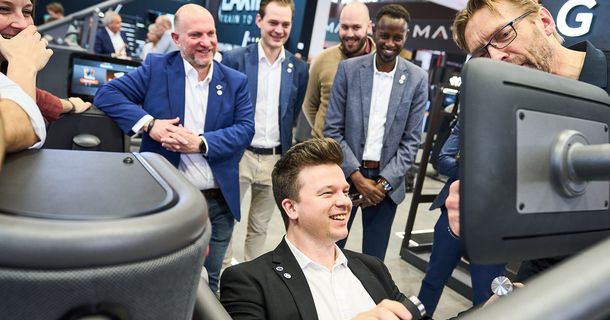 mann testet ein Fitnessgerät vor vielen strahlenden Gesichtern