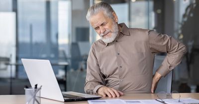 Älterer Mann mit Rückenproblem sitzt am Schreibtisch