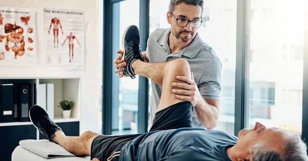 Physiotherapeut behandelt Knie von einem Mann, der auf einer Liege liegt