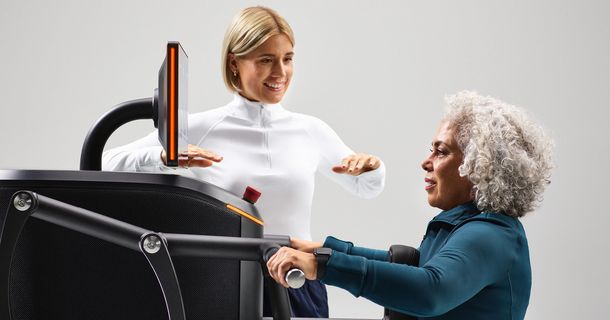 Eine Trainerin begleitet eine ältere Kundin lächelnd beim gesundheitsorientierten Krafttraining an einem vernetzten EGYM Smart Strength Gerät.