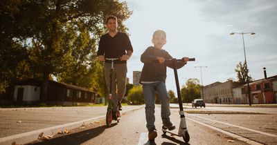 Ein Vater fährt mit seinem Sohn Tretroller