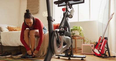 Frau bindet sich die Schuhe, im Vorfeld ist ein Peloton-Bike zu sehen