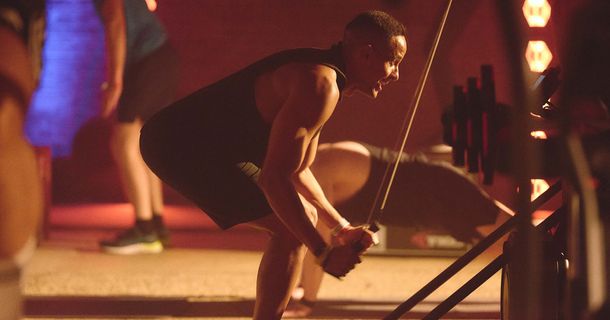 Dynamisches Ausdauertraining am SkiErg in einer Group-Fitness-Class mit weiteren Personen beim Krafttraining im Hintergrund.