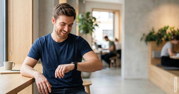 Mann im T-Shirt blickt auf seine Smartwatch
