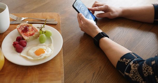 Person sitzt beim Frühstück und prüft ihre Gesundheitsdaten mit dem Polar A360