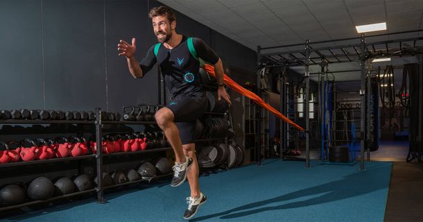 Mann trainiert im Fitnessstudio an einem Gummiband mit einem EMS-Anzug