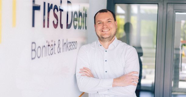 Mann mit verschränkten Armen lächelnd neben First Debit Schriftzug
