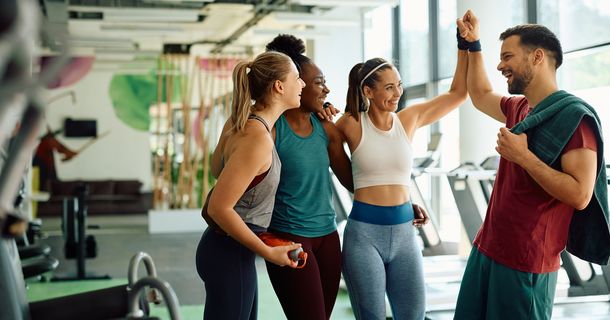 Fitnessstudiomitglieder geben dem Trainer ein High Five auf der Trainingsfläche