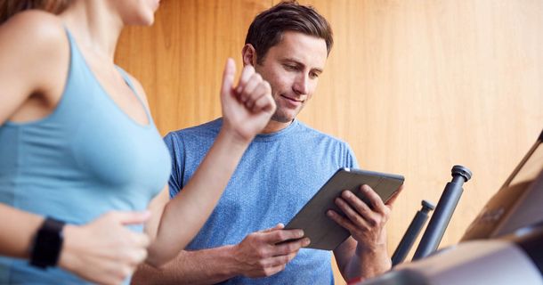 Datenerhebung bei einem Training durch einen Trainer mit laptop während eine Frau auf dem Laufband trainiert