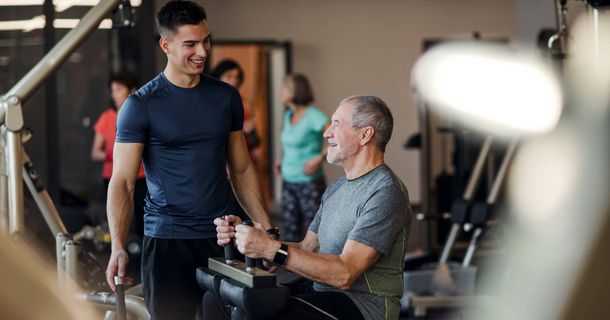 Trainer mit Senior beim Fitnesstraining am Gerät