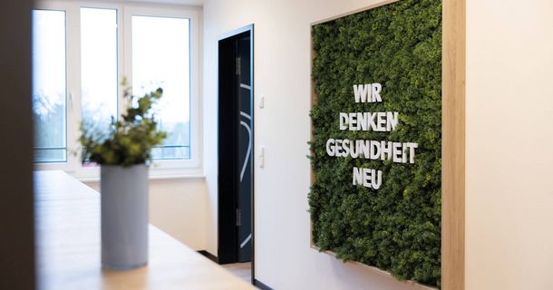 Praxiseingang mit Pflanzen und Schriftzug an der Wand