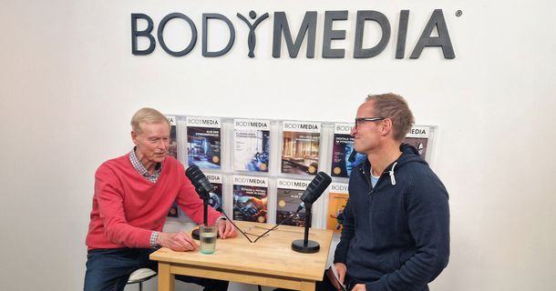 Hubert Horn sitzt im BODYMEDIA Interview an einem erhöhtem Tisch mit zwei Mikrofonen. 