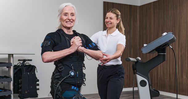 Grauhaarige Frau mit EMS-Weste und Trainerin