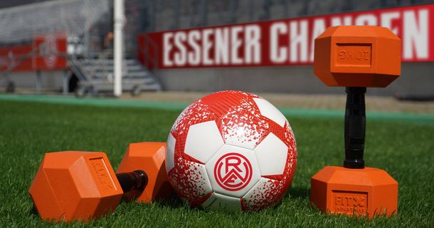 Fußball und Hanteln auf Rasen vor Bande mit Aufschrift „Essener Chancen"