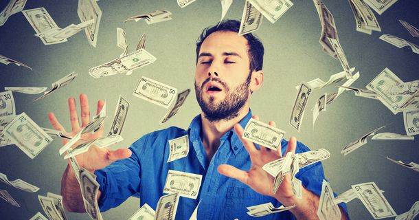 Ein junger, bärtiger Mann mit einem blauen Hemd steht mit geschlossenen Augen und offenen, nach vorne gestreckten Händen da, während zahlreiche Banknoten (US-Dollar) um ihn herum in der Luft fliegen oder auf ihn herabregnen. Die Szene symbolisiert Reichtum, finanziellen Erfolg oder einen Geldregen. Der Hintergrund ist ein schlichter, graublauer Farbverlauf.