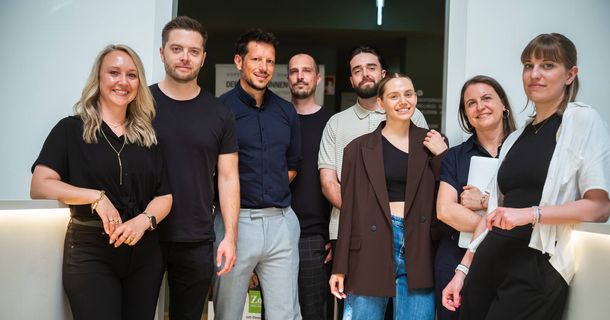Ein achtköpfiges Team aus Frauen und Männern steht nebeneinander und lächelt in die Kamera.