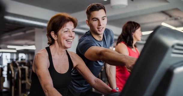 Junger Mann deutet auf das Display eines Trainingsgerät und zeigt einer lächelnden Frau etwas