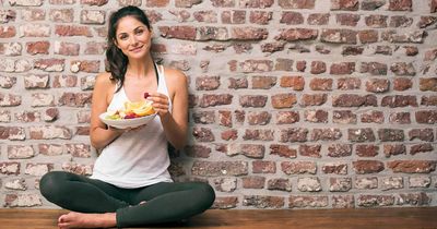 Frau mit Essen im Schneidersitz vor Steinwand