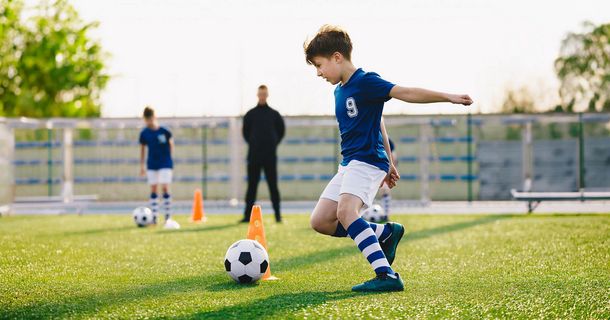 Junge trainiert auf dem Fußballplatz unter den Augen seines Trainers