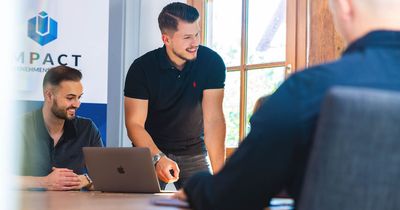 Maurice Leibinn am Schreibtisch mit weiteren Mitarbeitern. Er lächelt, im Hintergrund Impact-Logo