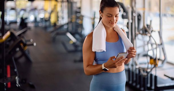 Eine fröhliche, sportliche Frau, die im Fitnessstudio trainiert und dabei auf ihrem Handy tippt.