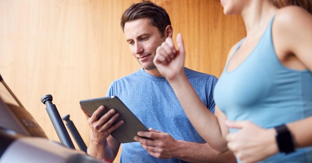 Mann mit Tablet neben einer laufenden Frau auf dem laufband