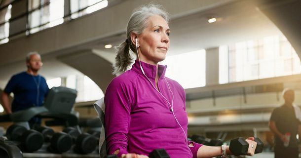 Frau mit grauen Haaren und pinkem Oberteil im Fitnessstudio