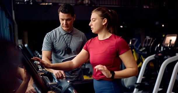 Personal Trainer überwacht das Lauftraining einer jungen, sportlichen Frau auf dem Laufband während des Trainings im Fitnessstudio.