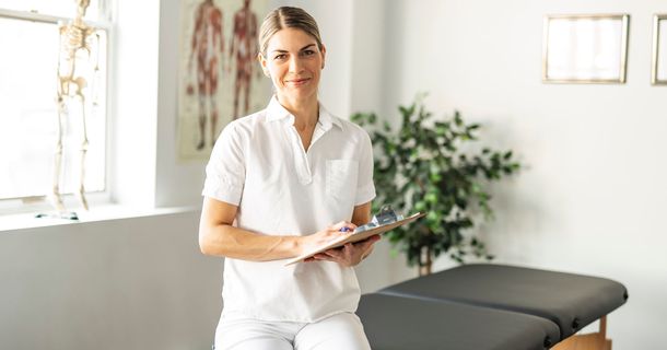 Physiotherapeutin sitzt auf Behandlungsliege und blickt positiv in die Zukunft