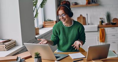 Junge Frau sitz lachend und mit Kopfhörern vor dem Laptop