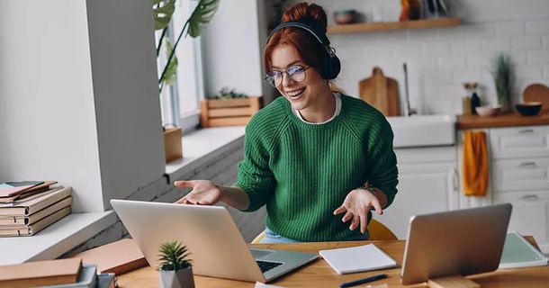 Junge Frau sitz lachend und mit Kopfhörern vor dem Laptop