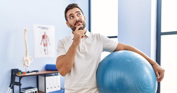 Ein Physiotherapeut hat einen Gymnastikball in der Hand und blickt hoch in die Luft