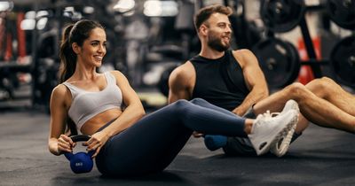 In einem Fitnessstudio sitzen zwei Sportler mit einem Klettlebell auf dem Boden.