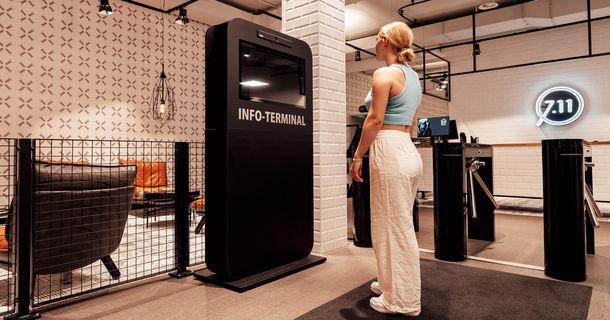 Fitnessstudiomitglied steht vor einem Info-Terminal in einem FITSEVENELEVEN-Fitnessstudio