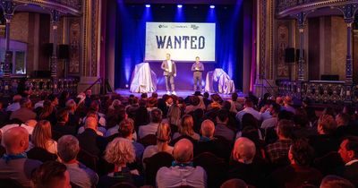 Publikum blickt auf die Bühne, auf der Wolf Harwath und Bernhard-Stefan Müller stehen, auf der Leinwand dahinter steht "WANTED"