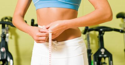 Frau misst ihren Bauch mit Maßband