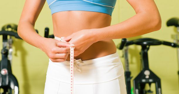 Frau misst ihren Bauch mit Maßband
