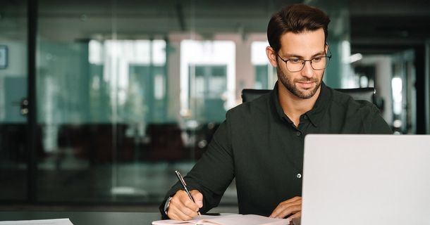 Person sitzt vor einem Laptop und nimmt an einem Webinar teil. Er macht sich Notizen